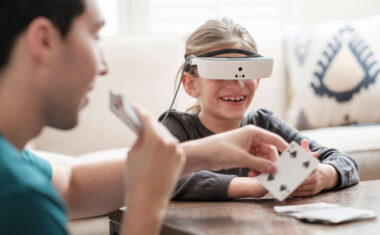 Young girl wearing eSight glasses holding cards in her hand playing with a man