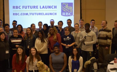 A group of Young Leader attendees standing in front of a projector with the RBC Future Launch Logo on it