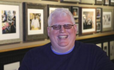 Dave Brown standing wearing transitional sunglasses smiling at the camera