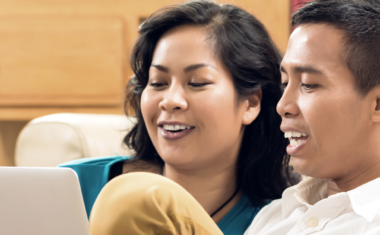 photo of a couple on a couch looking at a screen smiling