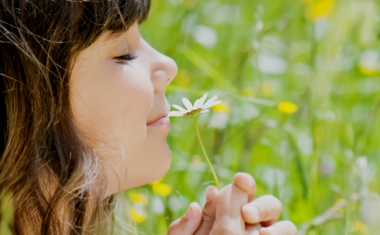 close up of girl smelling a flower in green field