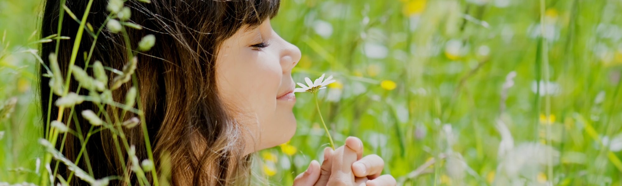 close up of girl smelling a flower in green field