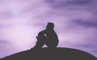 image of dark outline of a person sitting on a rock looking up at a cloudy sky