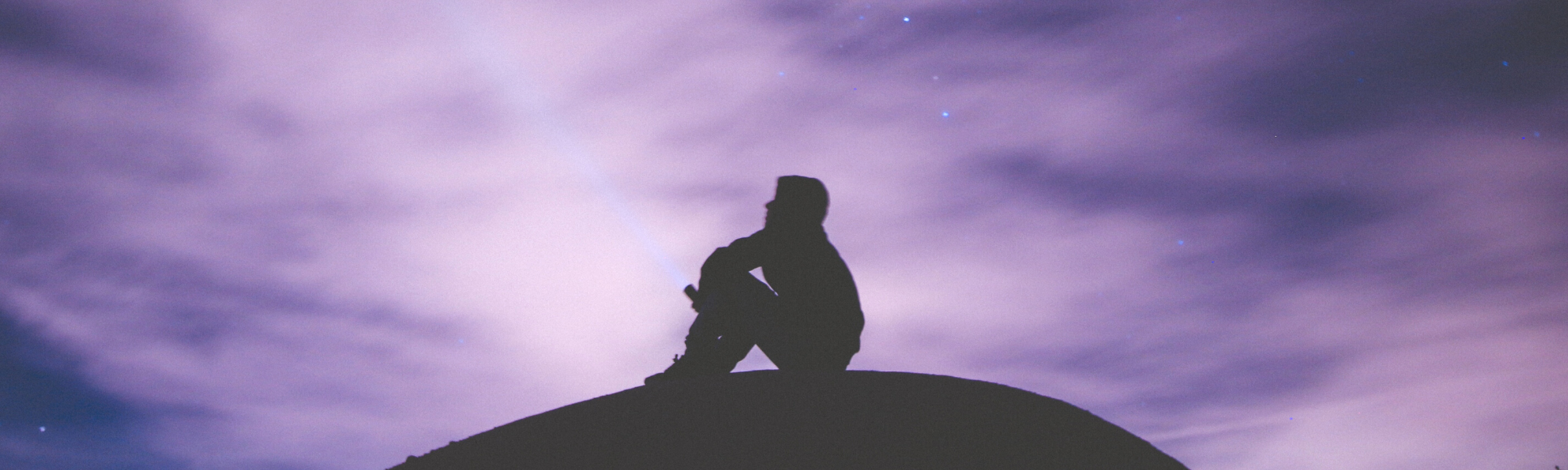 image of dark outline of a person sitting on a rock looking up at a cloudy sky