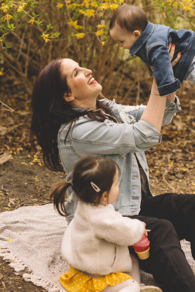 Image is of Shari of white cane story holding her baby, with her daughter seated next to her in the foreground.