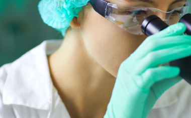 Image is of medical researcher looking through a microscope.