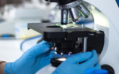 Image is of medical researcher in lap looking through a microscope