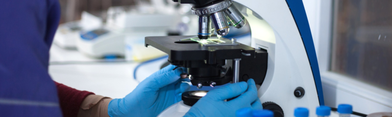 Image is of medical researcher in lap looking through a microscope