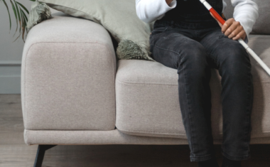 Image is of a woman seating holding a white walking cane