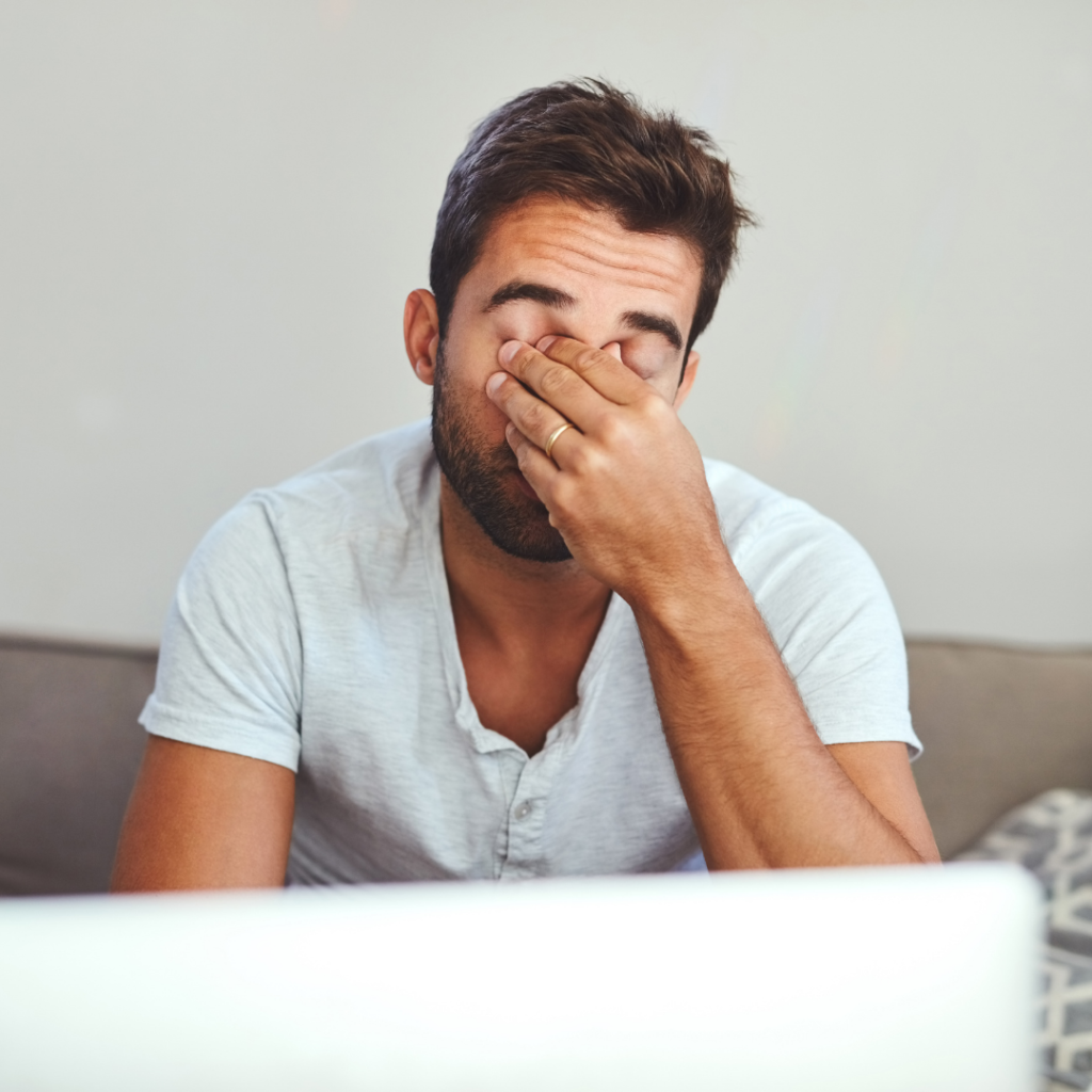 Image of man seated in front of a computer rubbing his eyes from eye strain