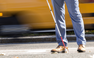 Image is of a professional man walking using a white cane