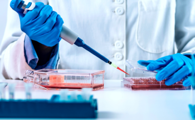 Image is of a lab tech using a medical device to interact with cells in a dish