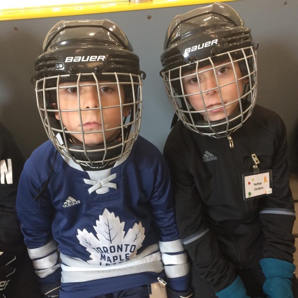 Image is of Luxturna recipients, Andre and Nathan. They are wearing hockey masks, a maple leafs jersey, and and sports gear