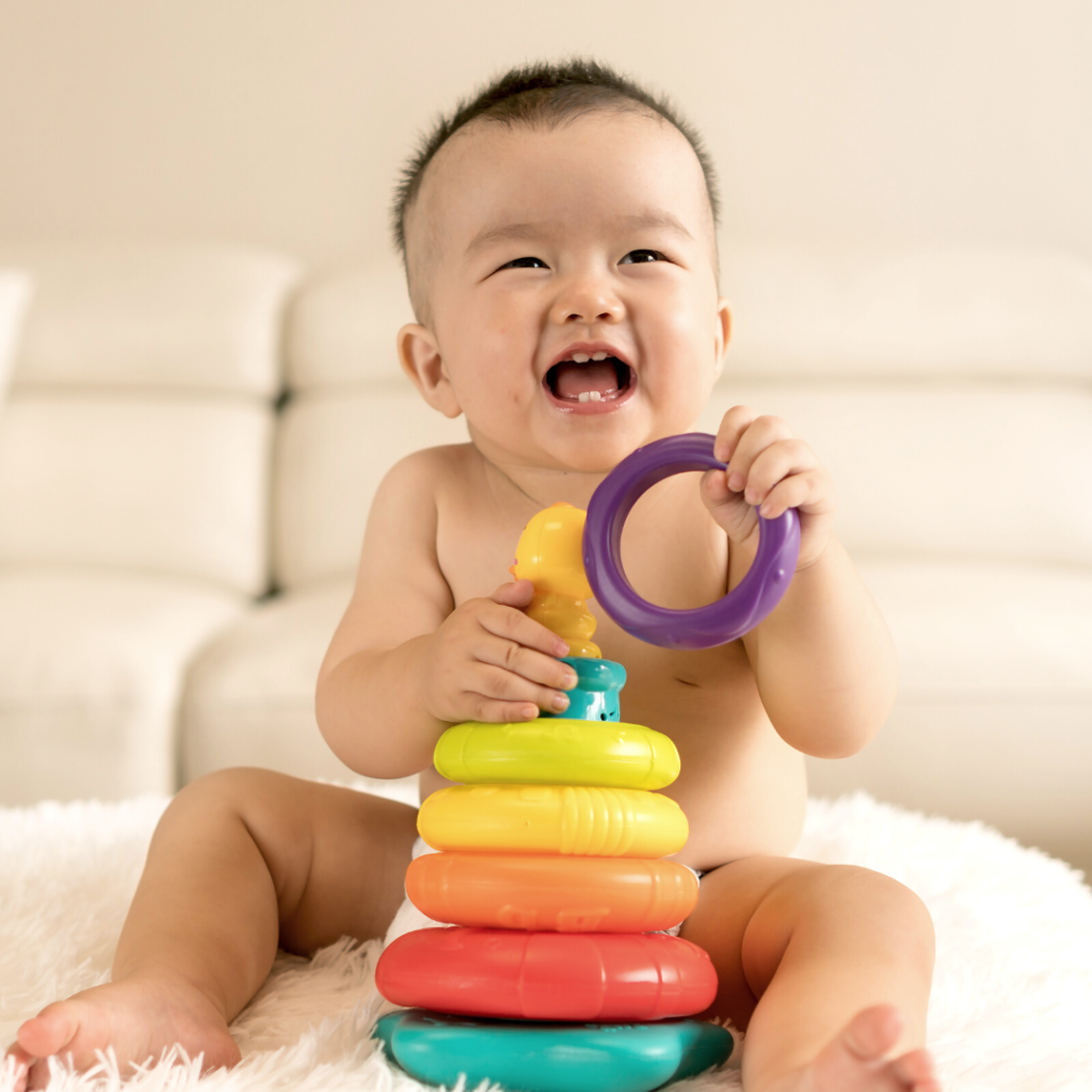 Image is of a baby smiling and playing with stacking toys