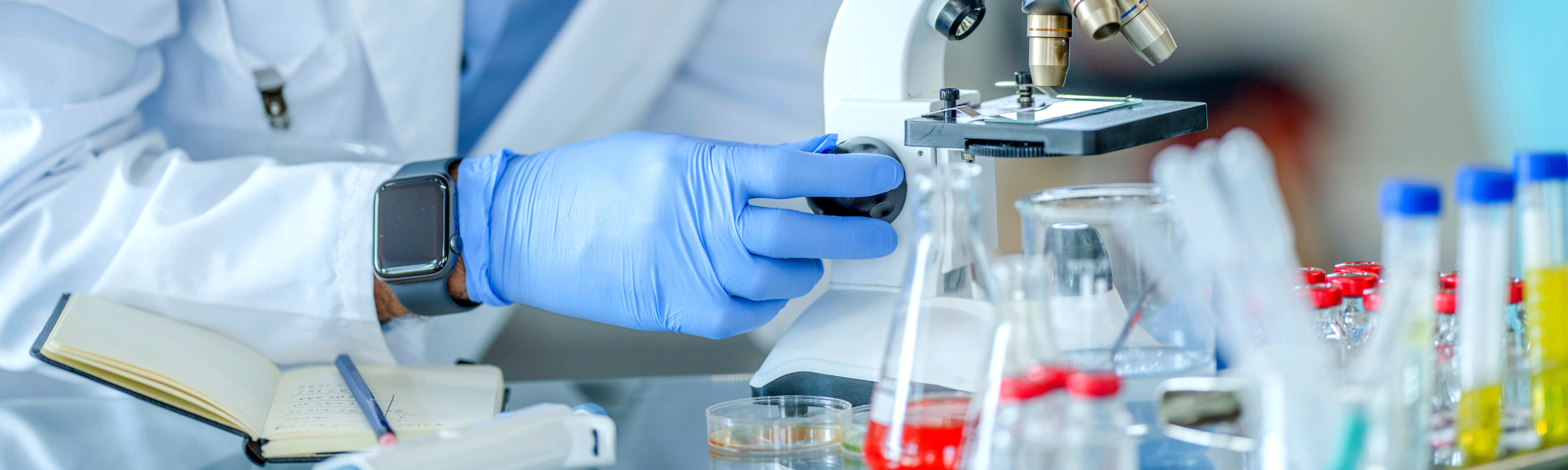 Image is of a lab tech looking through a microscope.