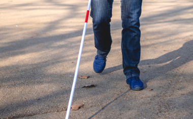 Image is of a man walking using a white cane.