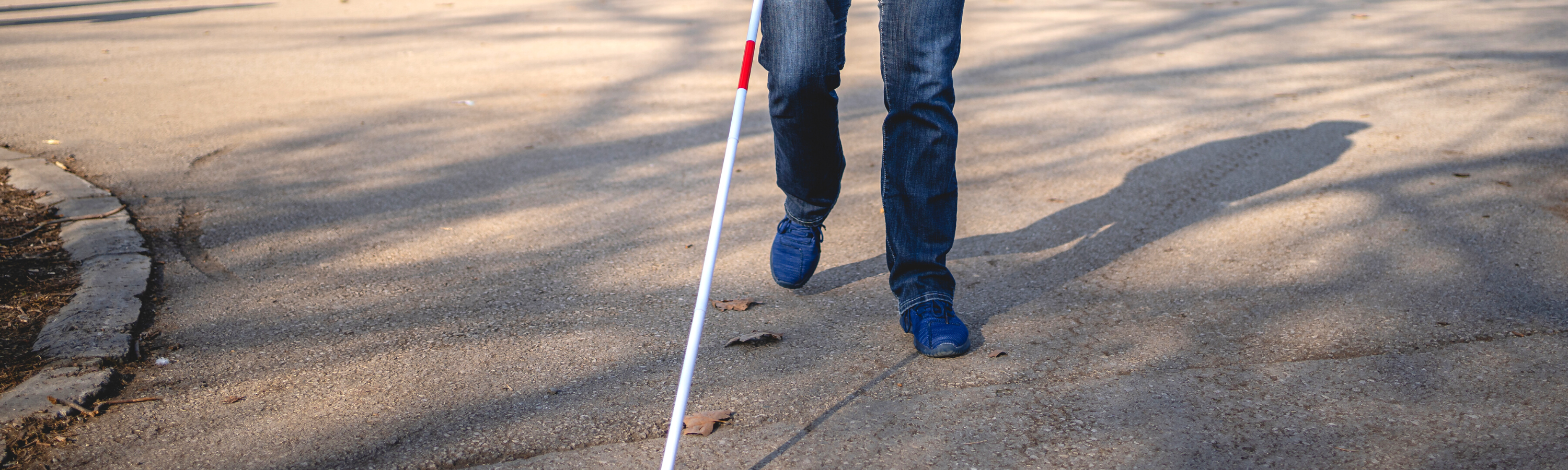 Image is of a man walking using a white cane.