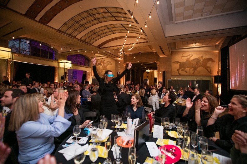 Image is of a group of people laughing at an event and clapping.