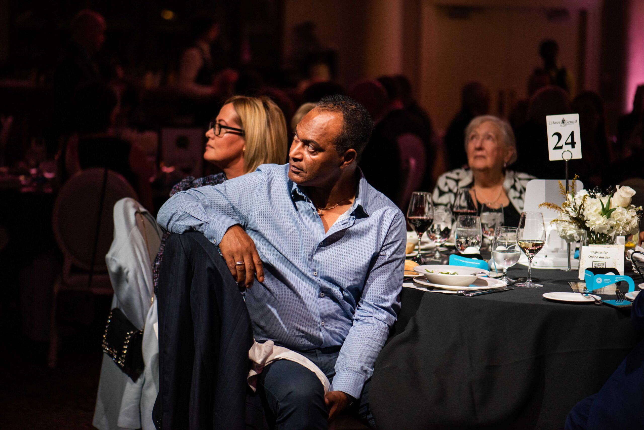Image is of a Comic Vision event attendee listening to a guest speaker while seated at dinner.