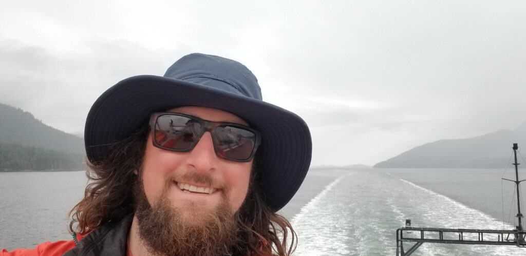 Image is of Cody Campbell smiling with a water body and mountains in the background.