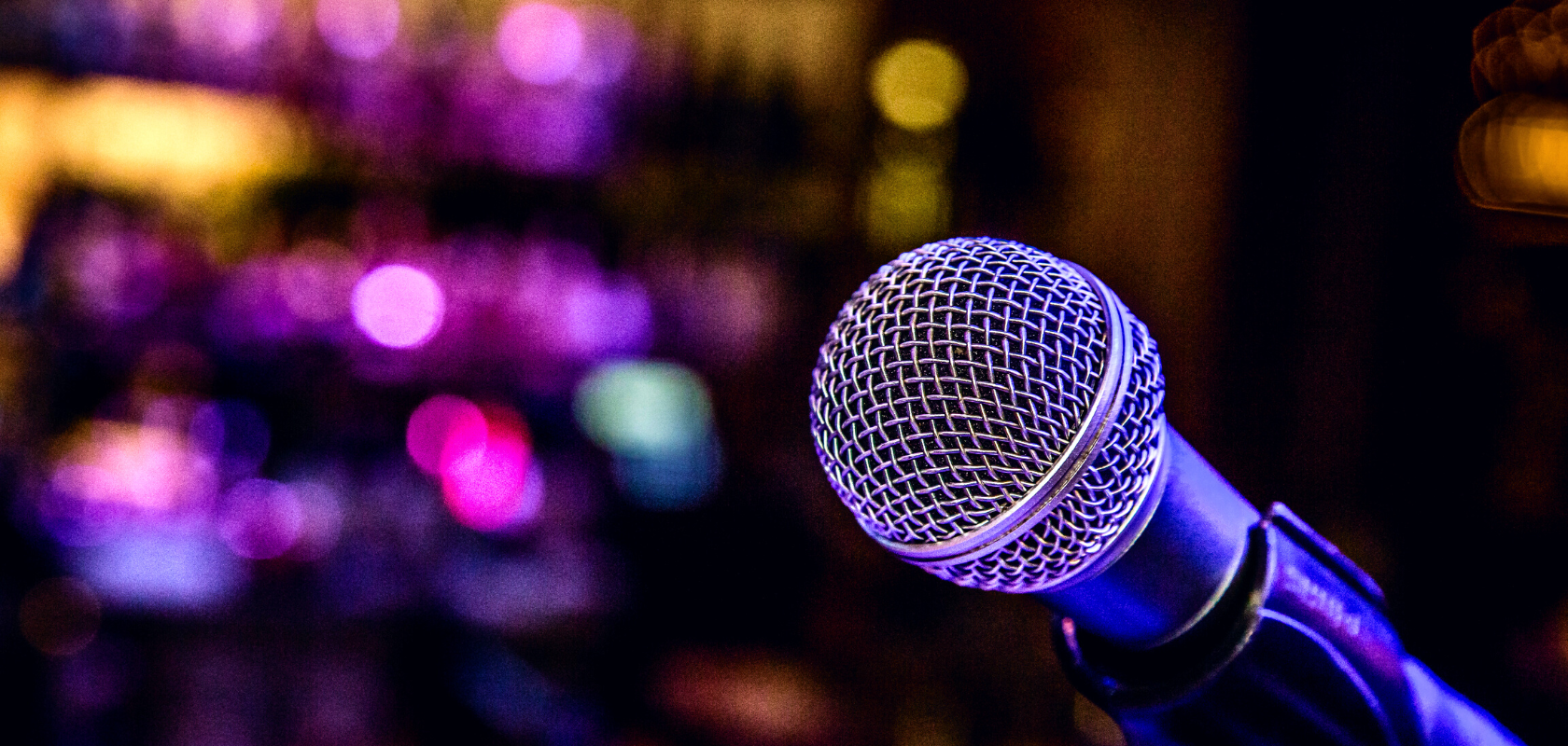 Image of a microphone in front of a dimmed light background with colourful lights.