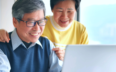 Image is of a mature couple smiling while looking at their laptop.