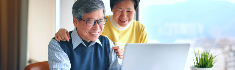 Image is of a mature couple smiling while looking at their laptop.