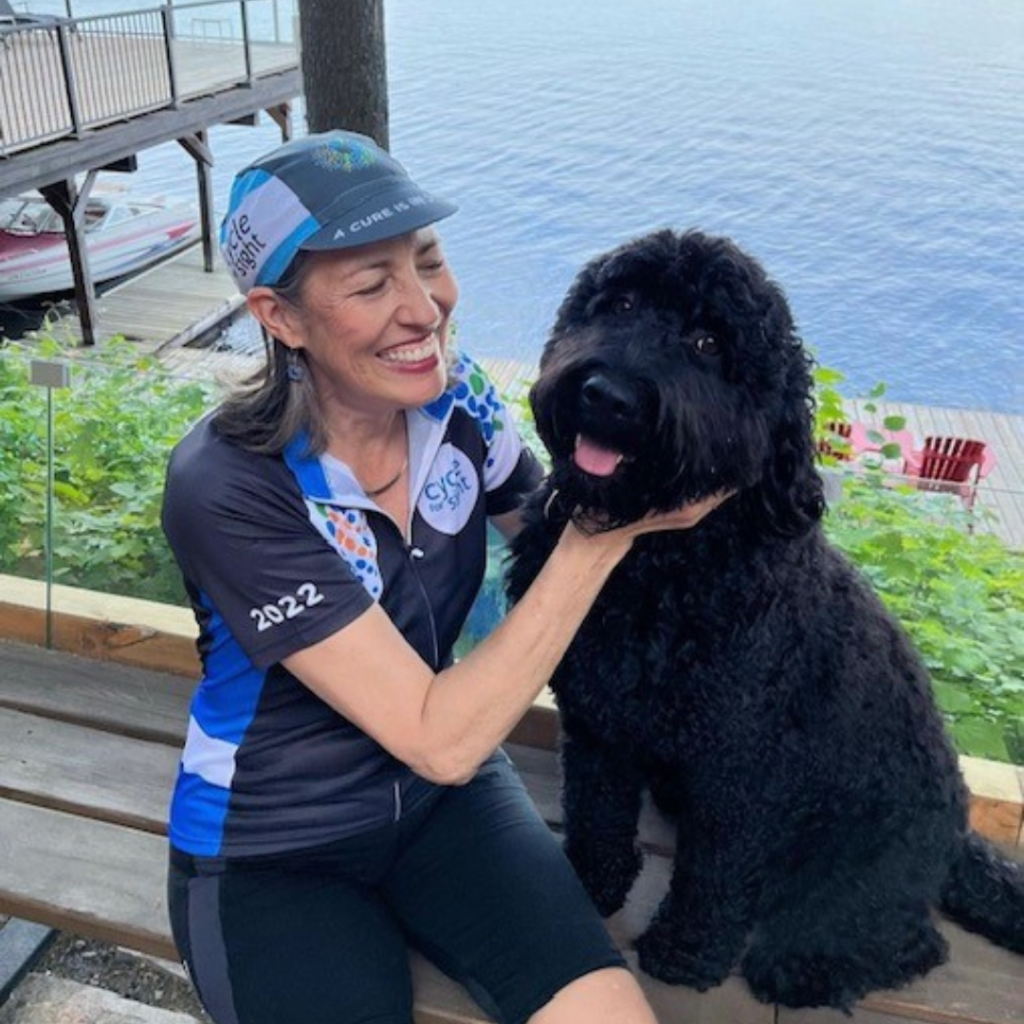 Image is of Ann Morrison petting a dog at a Cycle For Sight event. She is smiling.