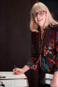 Image is of a woman participating in the Comic Vision auction while smiling for the camera.