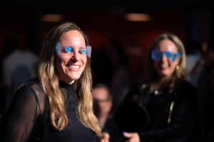 Image is of two women smiling wearing specialty glasses during the on-off glasses game held during Comic Vision.