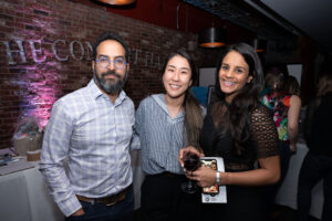 Image is of three Comic Vision event attendees. They are standing and smiling holding. One person is holding a beverage.