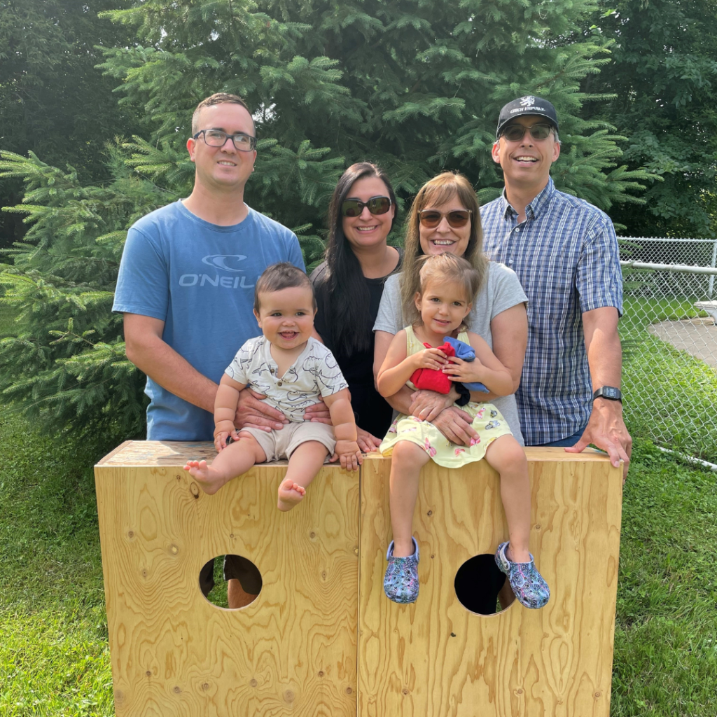 Image is of Amélie Savard-Lapointe and her family in front of two corn hold stations.