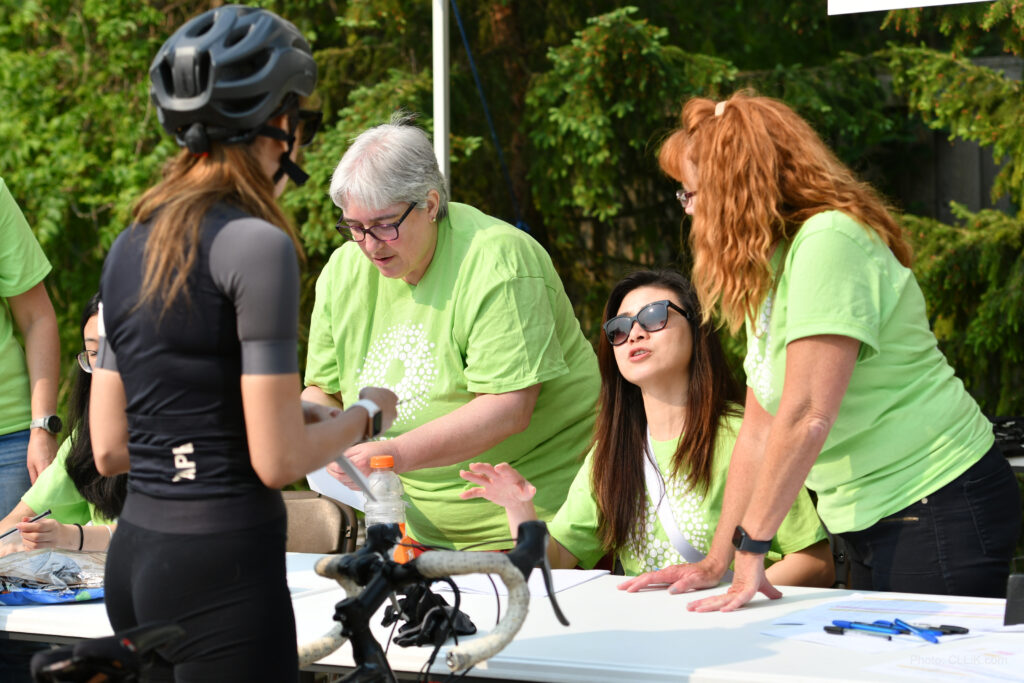 Volunteers speaking to riders behind a welcome table.