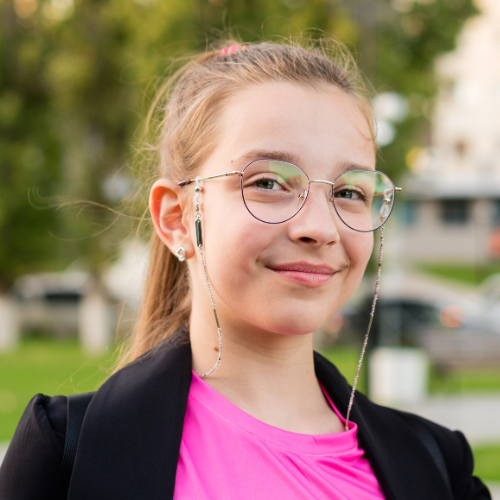 Girl out side wearing glasses, smiling at the camera