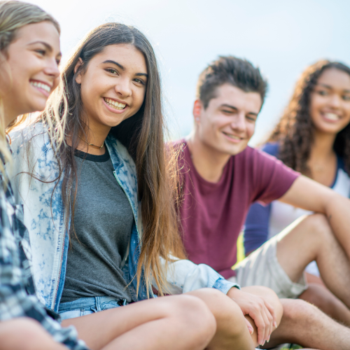 Group of teens sitting outside smiling.