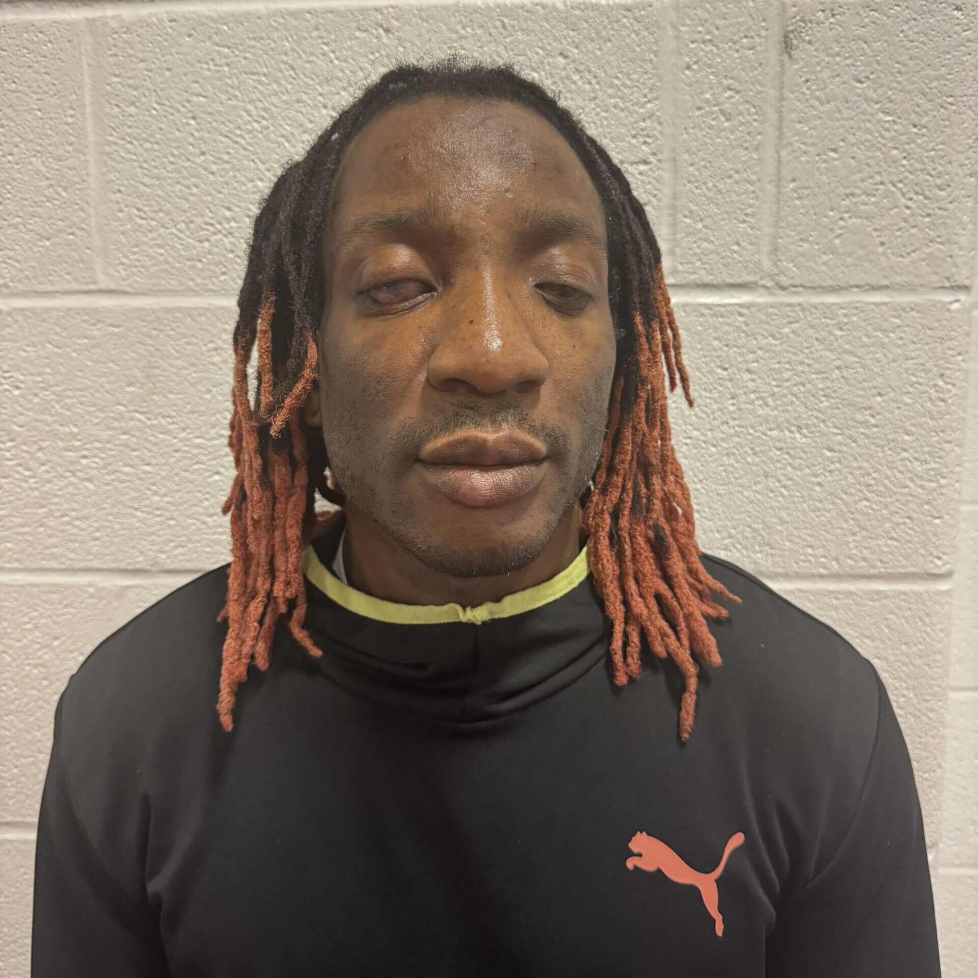 Image of George Quarcoo wearing a black shirt with a red puma on it standing in front of a white wall.