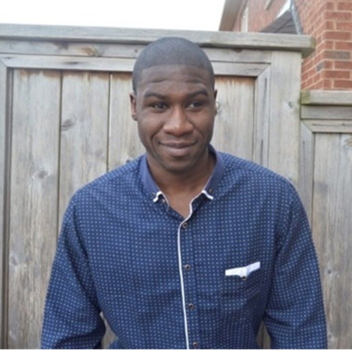 Image of Ben Akuoko in front of a wooden fence wearing a blue shirt